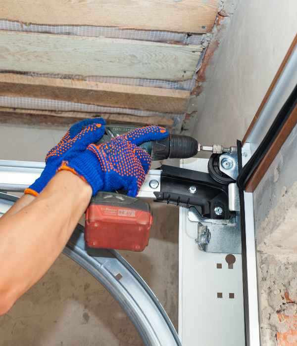 man wearing gloves fixing a garage door with a drill equipped with a screw driver bit